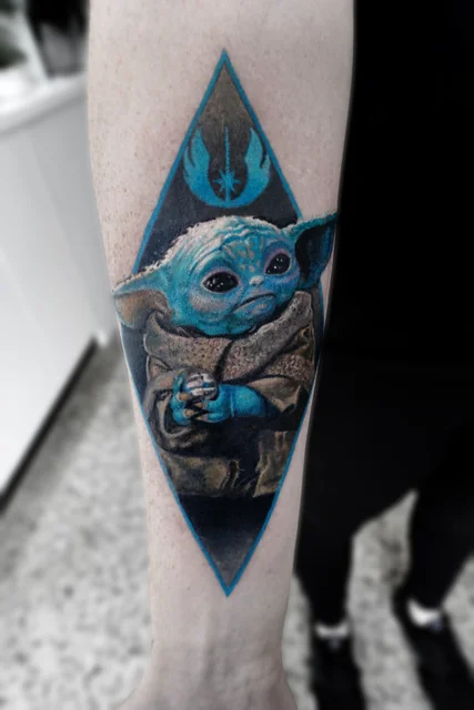 Colour Grogu tattoo framed by a blue diamond and emblem.