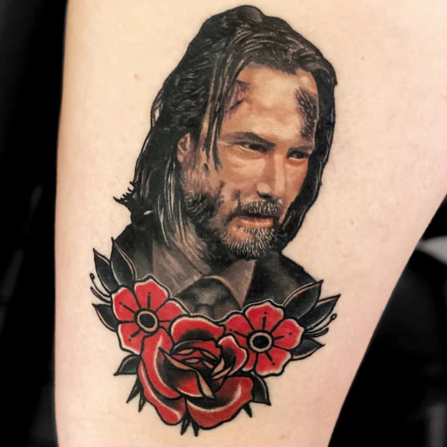 Keanu Reeves portrait tattoo above a red rose and smaller red flowers.
